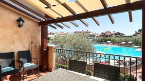 Ein Balkon mit Blick auf ein Schwimmbad, Sitzgelegenheiten im Freien und einer Pergola.
