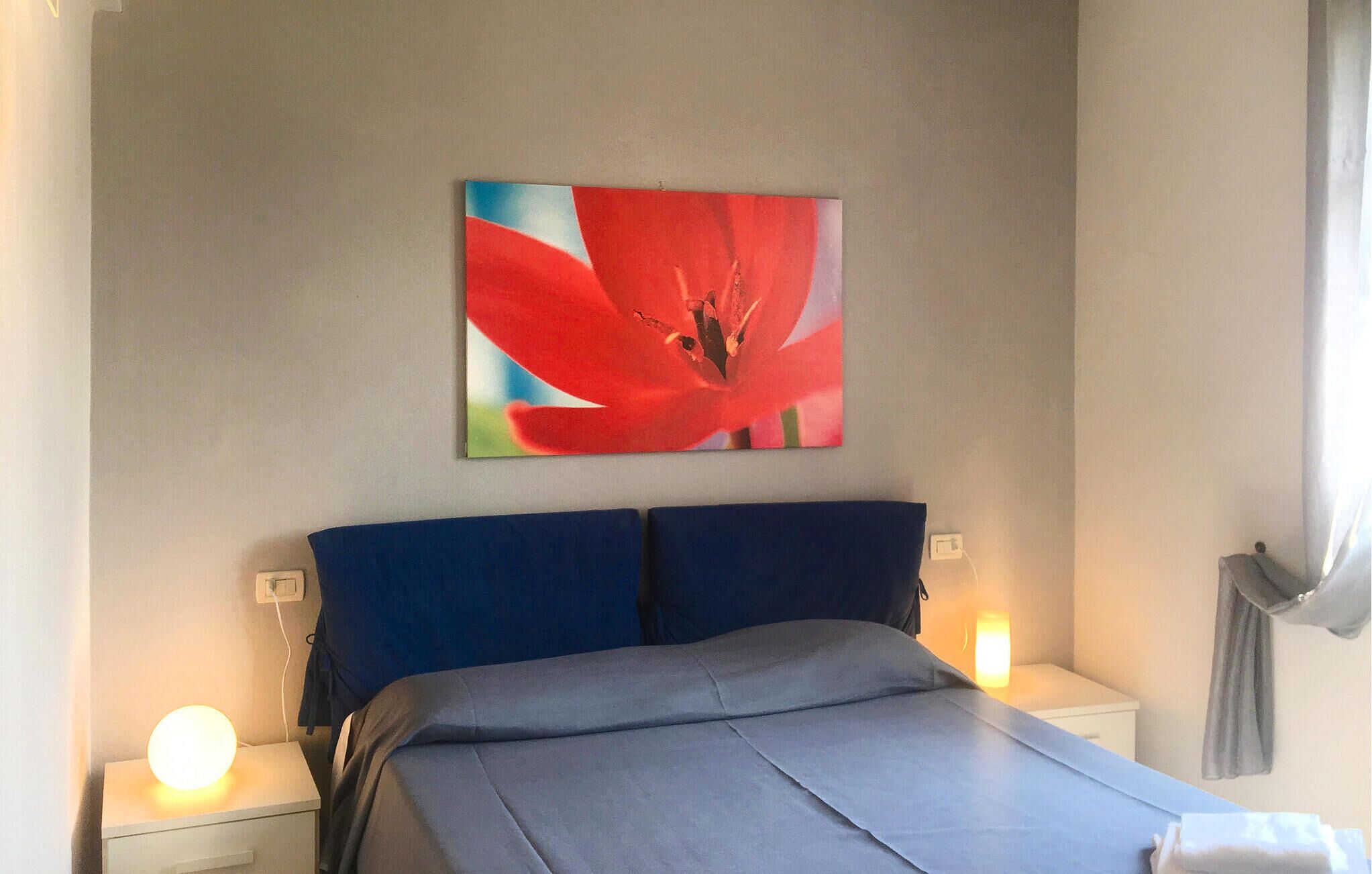A bedroom with a bed, two bedside tables, and a wall-mounted painting of a red flower.