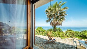 A view from a window overlooking a beach with a palm tree, a chair, and a rocky ground. - 2 bedroom nice home in Castelsardo (Castelsardo)