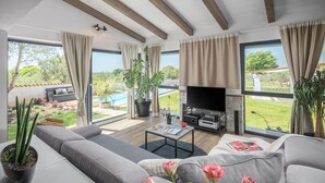 Un salon moderne doté d’un grand téléviseur, de sièges confortables et offrant une vue sur une piscine.