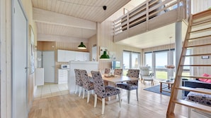 A spacious living area with a high ceiling, wooden flooring, a dining table with floral chairs, a loft bedroom with a wooden ladder, and large windows offering a view. - Stunning home in Faaborg with WiFi (Faaborg)