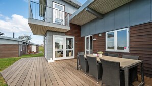 A modern house with a wooden deck, a dining area with wicker furniture, and a balcony. - Stunning home in Faaborg with WiFi (Faaborg)
