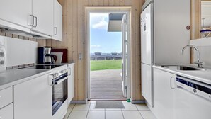 A modern kitchen with white cabinets, a built-in oven, a coffee maker, and a view of a residential area through a door. - Stunning home in Faaborg with WiFi (Faaborg)
