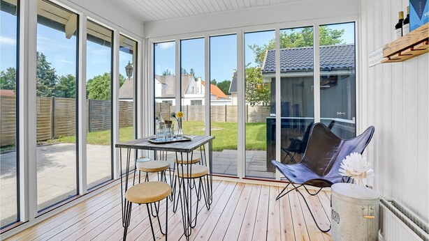 Un patio iluminado por el sol con una mesa de madera, cuatro taburetes altos, una silla plegable y una pequeña mesa redonda con un adorno.