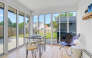 A sunlit patio with a wooden table, four bar stools, a folding chair, and a small round table with a decorative item. - Gorgeous home in Otterup with sauna (Otterup)