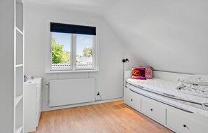 A small, well-lit room with a sloped ceiling, a window with a view of greenery, a bed with a white mattress and pillows, a bedside table with a lamp, and a radiator. - Gorgeous home in Otterup with sauna (Otterup)