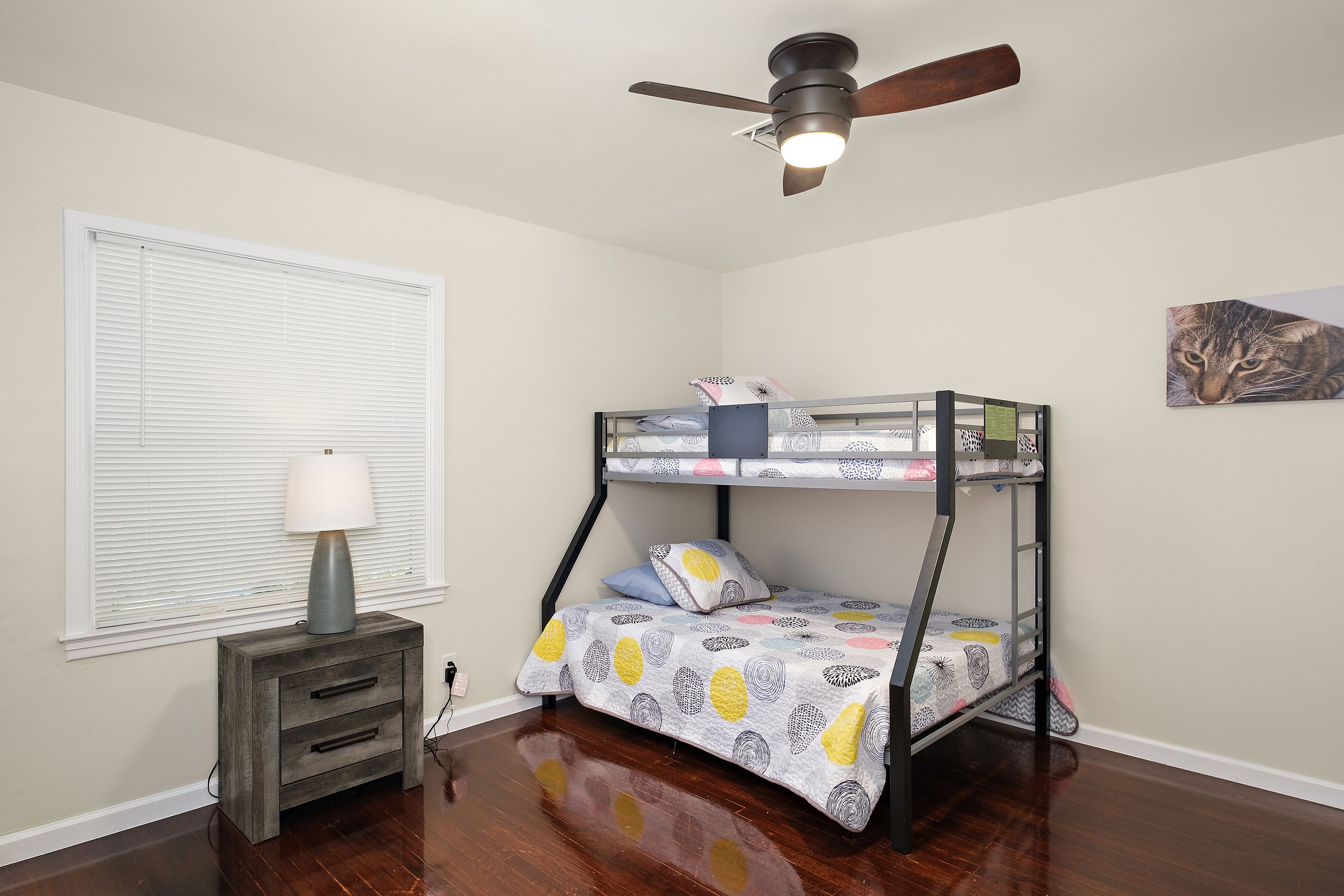 A bunk bed with a patterned bedspread, a bedside table with a lamp, and a ceiling fan.