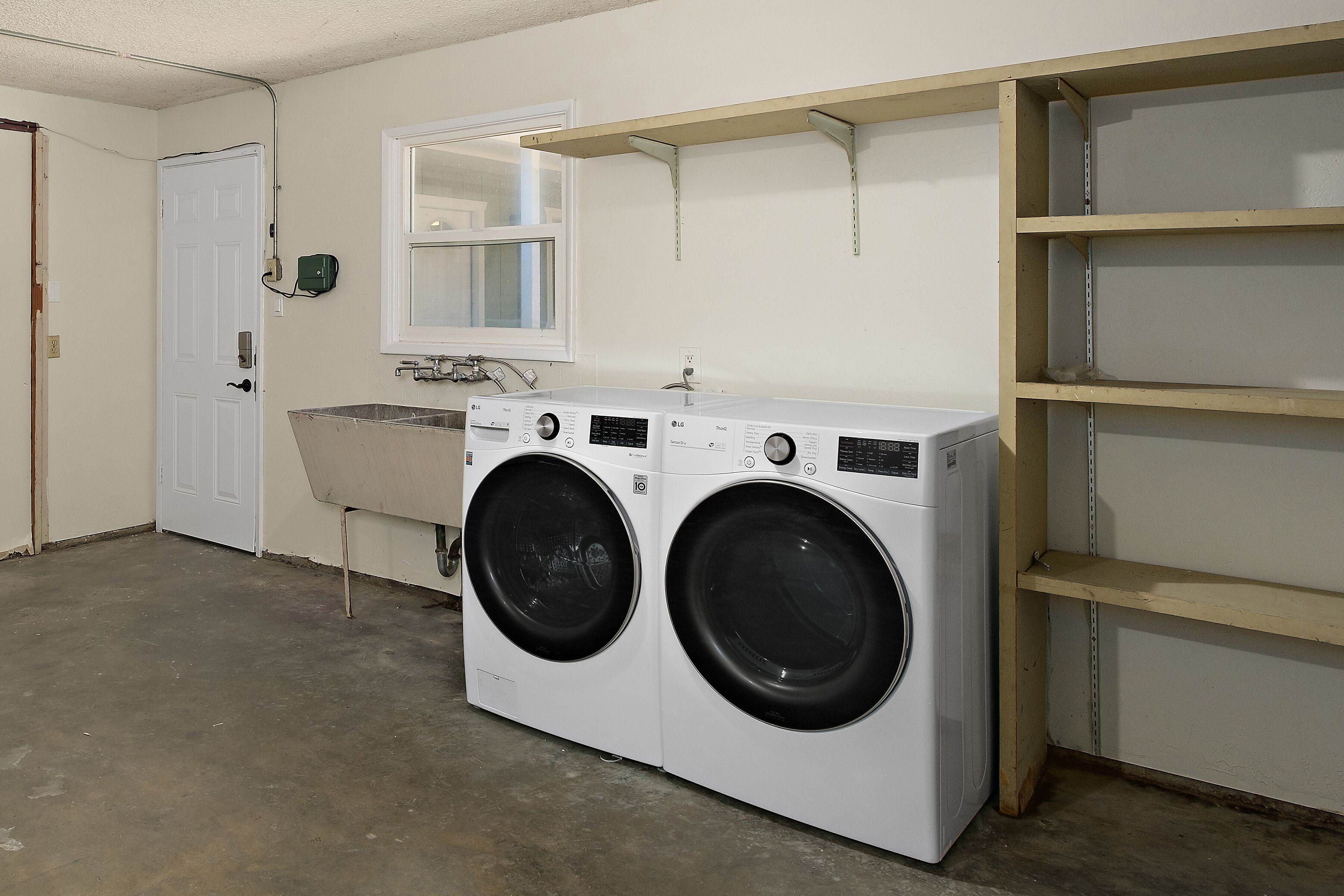A laundry room with a front-loading washer and dryer, a sink, and a mirror above the sink.