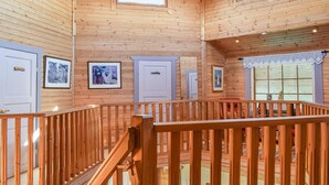 Een houten interieur met een houten balustrade, kunstwerken in lijsten aan de muren, en een raam met zonwering.