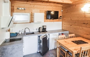 Eine kleine Küche mit Spüle, Kaffeemaschine und Mikrowelle. Ein Holztisch mit Stühlen steht bereit.