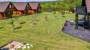Ein gepflegter Rasen mit einer Holzterrasse und einem Sitzbereich im Freien. Im Hintergrund sind mehrere Holzhütten mit roten Dächern zu sehen.