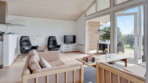 Amplia sala de estar con un ventanal, un sofá, dos sillones, un televisor y un comedor.