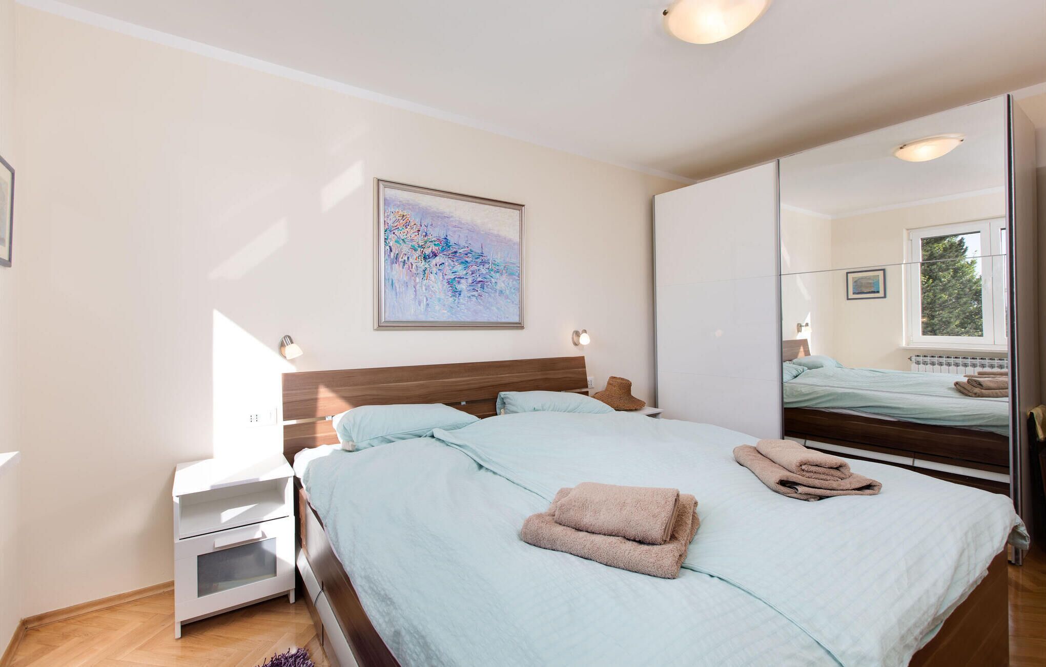 Une chambre à coucher avec un lit, une table de chevet, un miroir et un tableau accroché au mur.