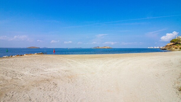 En sandstrand med en klar blå himmel, rolig sø og fjerne øer.