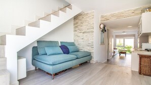 En moderne stue med en blå sofa, en væg med stenudsmykning og en trappe, der fører til et andet niveau.