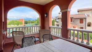Ein Balkon mit Tisch und Stühlen, mit Blick auf einen Innenhof mit Gebäuden und Grünflächen.
