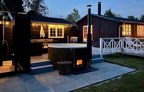 Una cabaña de madera con jacuzzi, mobiliario exterior y chimenea.