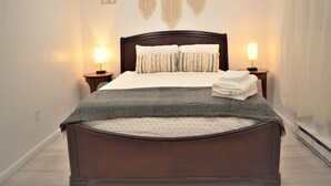 A neatly made bed with a dark wooden headboard, two bedside lamps, and a decorative macramé piece above. - Creek house with expansive mountain views (ashland)