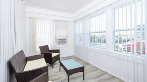 A room with wicker furniture, a radiator, and large windows with blinds. - Modern Beachfront Suite 309 (Ocean City)