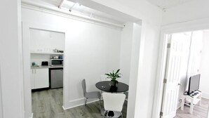 A modern kitchen with white cabinets, a microwave, and a small dining area with a table and chairs. - Modern Beachfront Suite 309 (Ocean City)