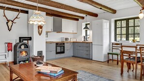 Een rustieke keuken met houten balken, een houtkachel en een eethoek met een houten tafel en stoelen.