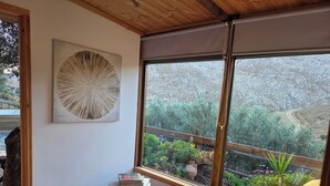 Une pièce dotée d’une grande fenêtre, d’un plafond en bois, d’une œuvre d’art murale de forme ronde, d’une petite table avec des livres, d’un canapé jaune et d’un tapis rouge à motifs.
