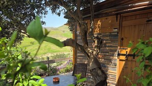 Une cabane en bois à l’aspect rustique, une table ronde surmontée d’un saladier en cuivre, et une vue sur un paysage verdoyant.