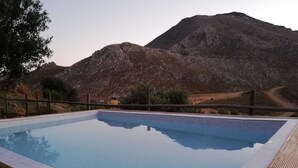 Une piscine rectangulaire entourée d’une terrasse en bois, le tout se fondant dans un paysage montagneux.