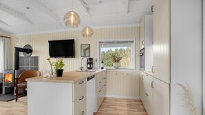 Una cucina moderna con isola centrale, pavimento in legno, piano cottura integrato, una finestra con vista e illuminazione a sospensione.