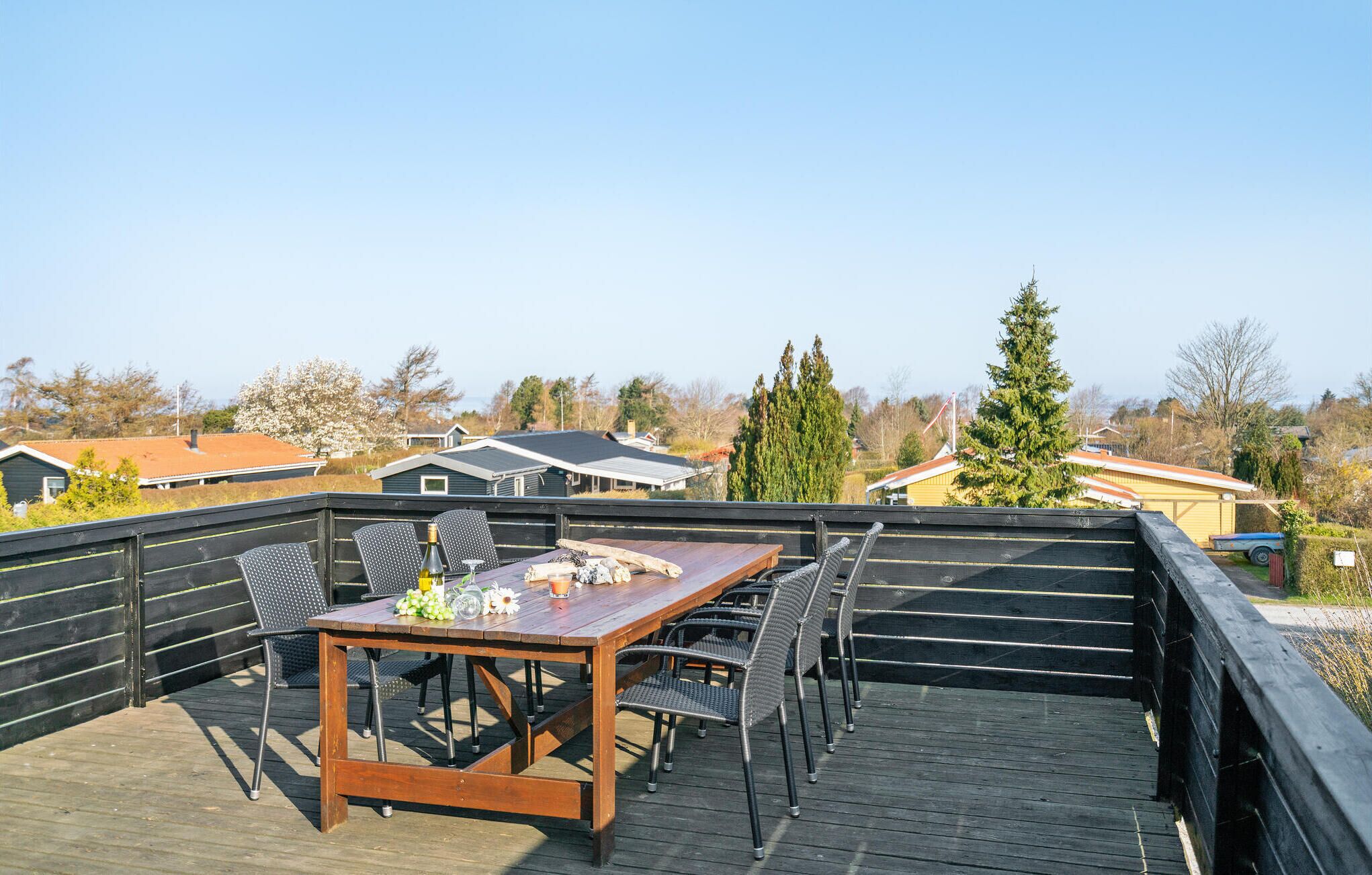 A wooden deck with a table and chairs, overlooking a residential area with houses and trees.