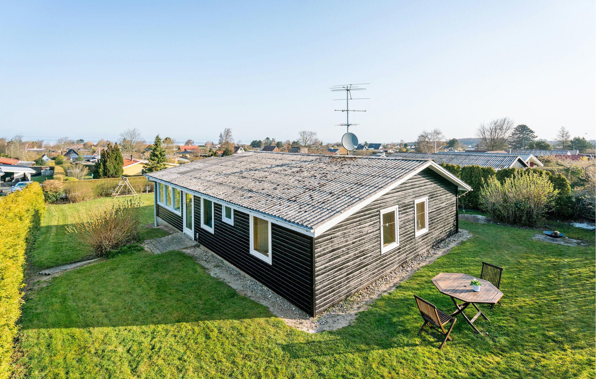 Ein kleines, eingeschossiges Holzhaus mit geneigtem Dach, einer Satellitenschüssel und einer kleinen Terrasse mit Tisch und Stühlen.