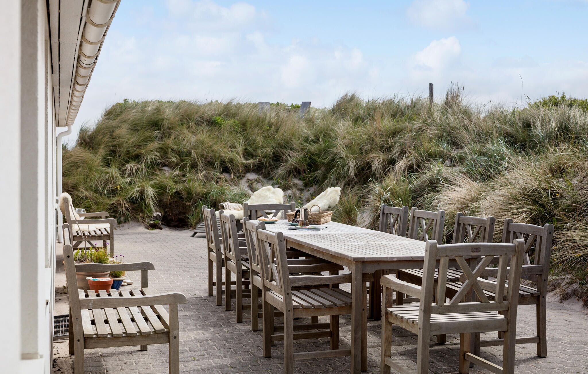 Un área de comedor al aire libre con mesas y sillas de madera, rodeada de dunas de arena y vegetación.