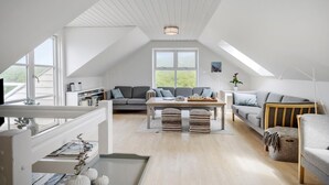 Spazioso loft con soffitto alto, zona living centrale con divani e tavolino, tavolo da pranzo e ampia finestra con vista sull'esterno.