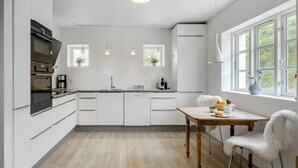 Una cucina moderna con mobili bianchi, un tavolo da pranzo in legno e vista sul verde dalle finestre.