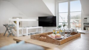 Un soggiorno moderno con un vassoio di legno che contiene snack e bicchieri, una televisione e un'ampia finestra con vista sull'esterno.