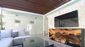 A modern outdoor living area with a glass table, white sofa, and a mounted TV. - Avida - Stunning Rooftop Pool and Jacuzzi (Puerto Vallarta)