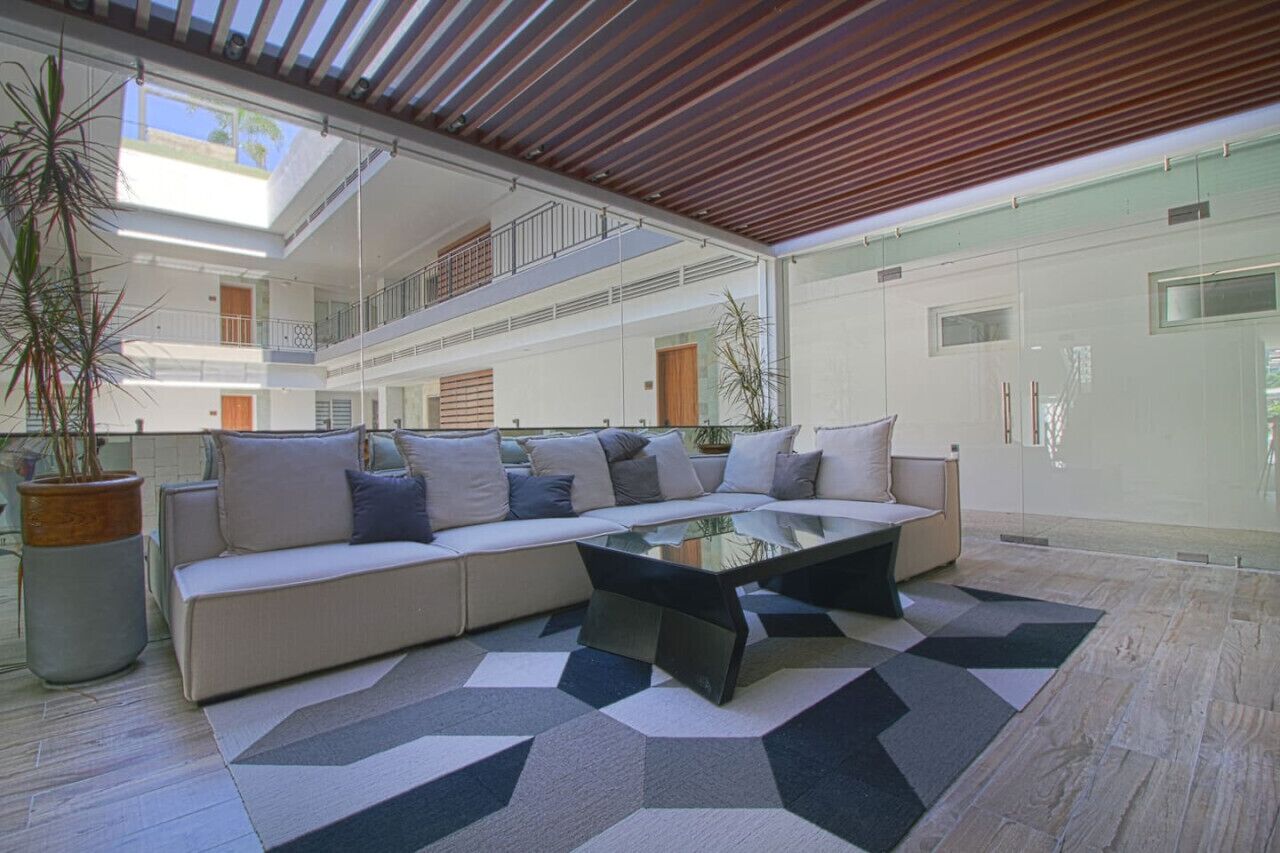 Un espace de vie spacieux et moderne, comprenant un canapé d’angle, une table basse en verre et un tapis à motifs géométriques.