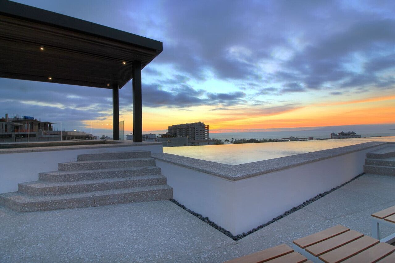 A rooftop terrace with a pool, steps leading to the pool, and a view of the sunset over the sea.