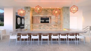 A modern dining area with a large rectangular table, white chairs, and geometric pendant lights. - Avida - Stunning Rooftop Pool and Jacuzzi (Puerto Vallarta)