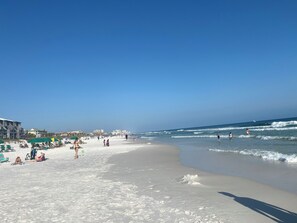 Ein Strand mit badenden und spielenden Personen, einem klaren Himmel und brechenden Wellen.
