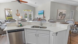 Una cocina moderna con lavavajillas integrado, una isla grande con pileta y un comedor con sillas estampadas.
