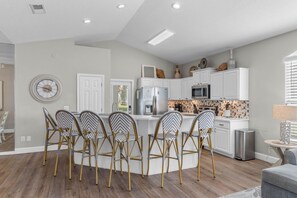 A modern kitchen with white cabinetry, a central island with bar stools, and a dining area with a round table. - “Beach Jewel” 5 bdrm , 3 1/2<br>bath home.  5 min walk to the beach (Destin)