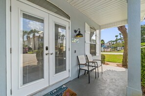 A covered porch with a sliding glass door, a bench, and a wall-mounted light fixture.