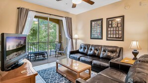 A living room with a TV, leather sofa, and a ceiling fan.