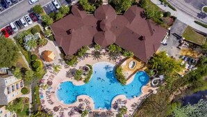 An aerial view of a hotel with a large swimming pool, multiple guest rooms, and a parking lot.