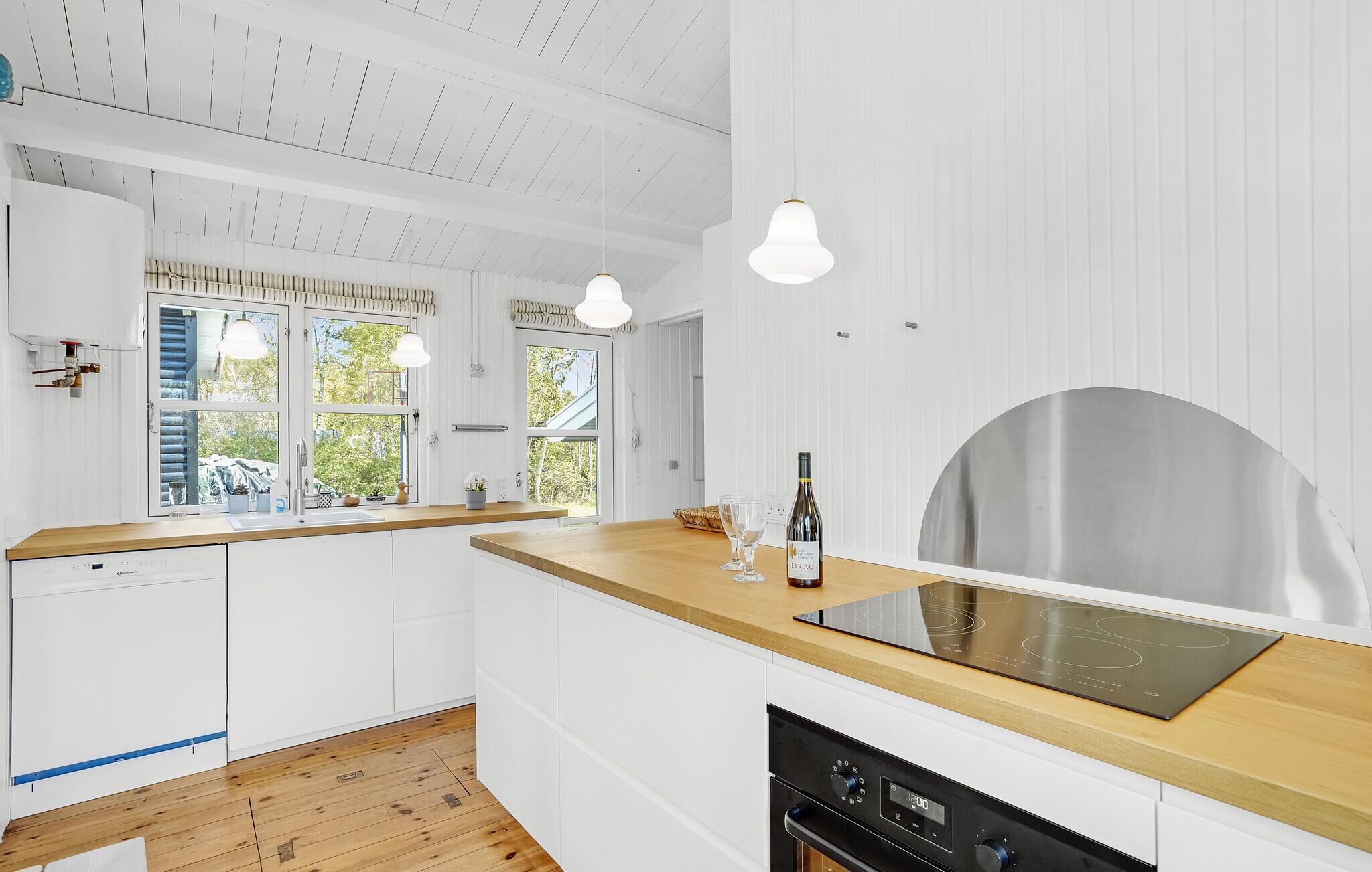 Une cuisine moderne avec des meubles blancs, un plan de travail en bois, un four encastré et une hotte en acier inoxydable.
