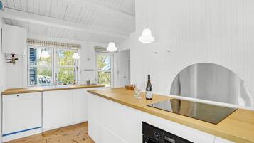 Une cuisine moderne avec des meubles blancs, un plan de travail en bois, un four encastré et une hotte en acier inoxydable.