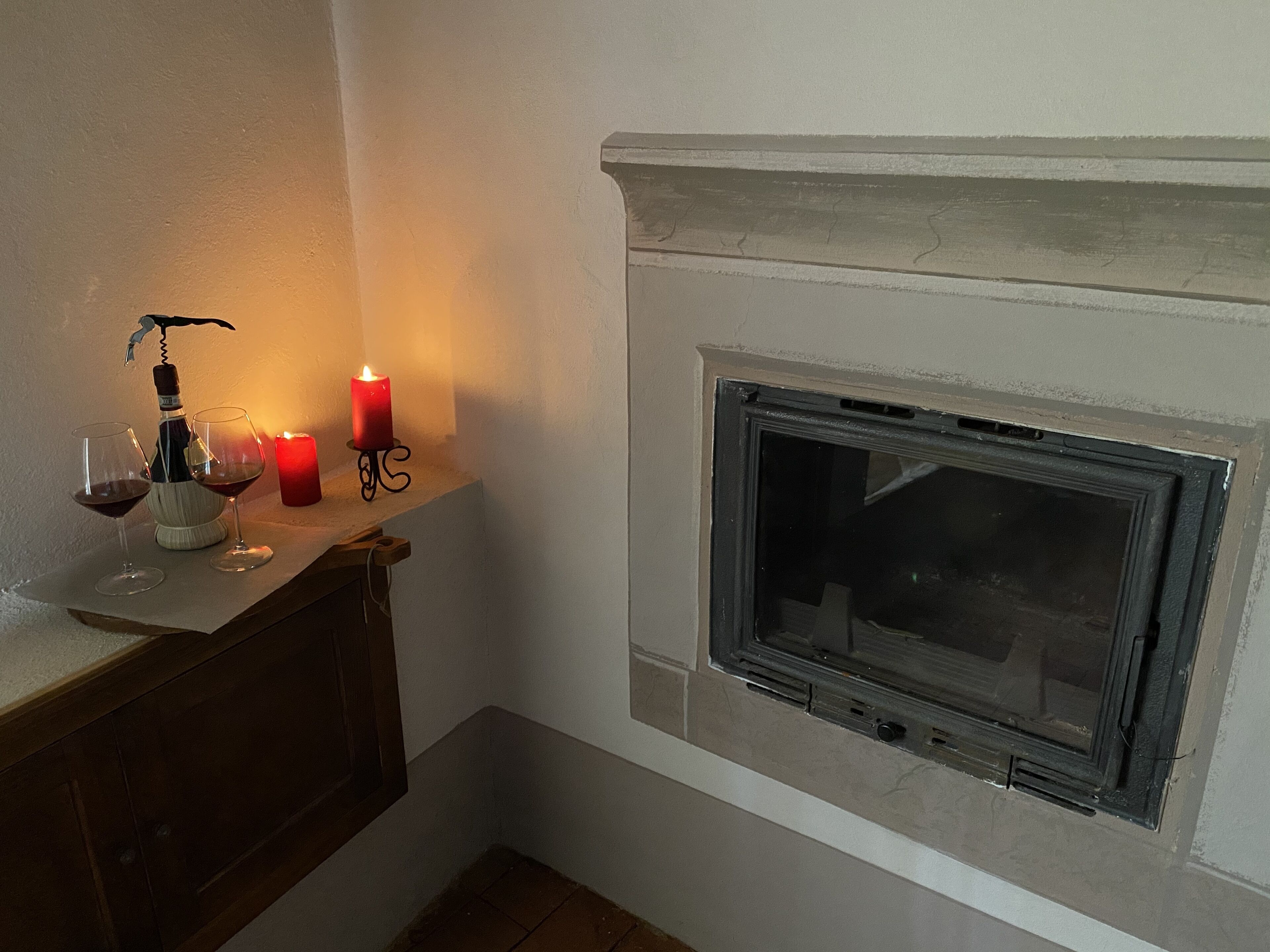 A fireplace with a stone mantle, a wine bottle, two glasses, and a candle on a mantelpiece.
