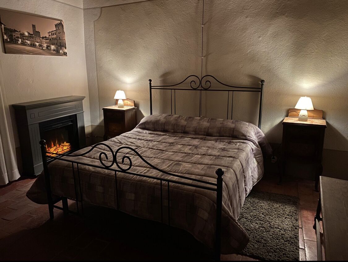 A bedroom with a metal bed frame, a fireplace, two bedside lamps, and a rug on the floor.