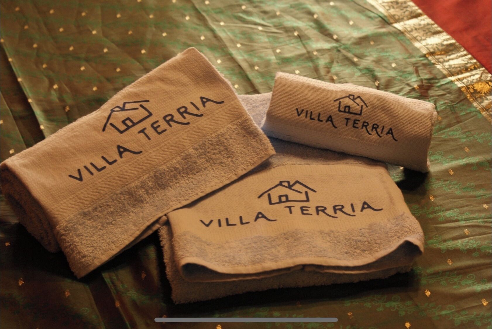 Tres toallas dobladas con el texto "Villa TERRA" y un icono de casa.
